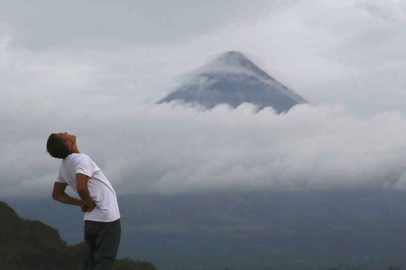 Seljak se proteže dok vulkan Mayon izbacuje pepeo i lavu u gradu Legaspi na Filipinima.