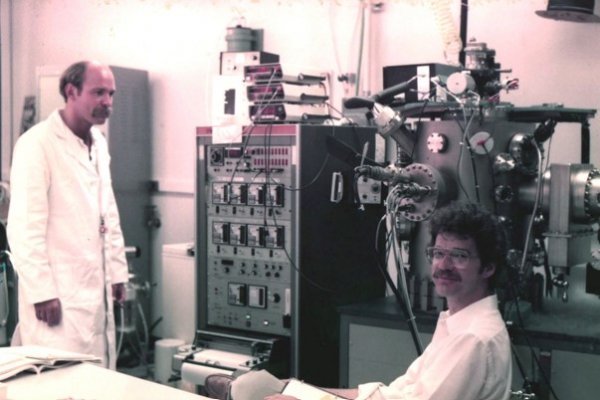 Doktorski student Mark Mondry (desno) i post-doc Ernie Caine ispred prototipnog MBE uređaja Varian 360 u laboratoriju (1984. godina).